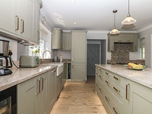 A modern kitchen with light-colored cabinets, a wooden floor, and pendant lighting. - The White House (Okehampton)