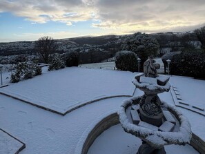 A snow-covered outdoor area with a statue, a paved path, and a distant view of a town. - The White House (Okehampton)