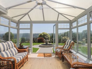A conservatory with wicker furniture, a glass table, and a view of a landscaped garden.