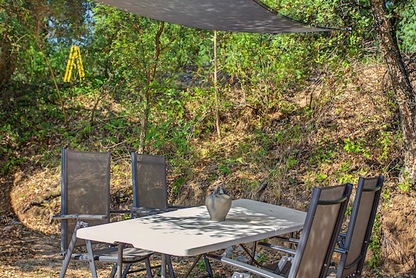 Juego de mesa y sillas al aire libre bajo un toldo, rodeado de follaje natural.