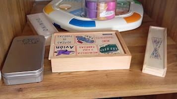 Una estantería de madera con un juego de mesa, una lata y una caja etiquetada 'JUEGO MAGISTRAL'.