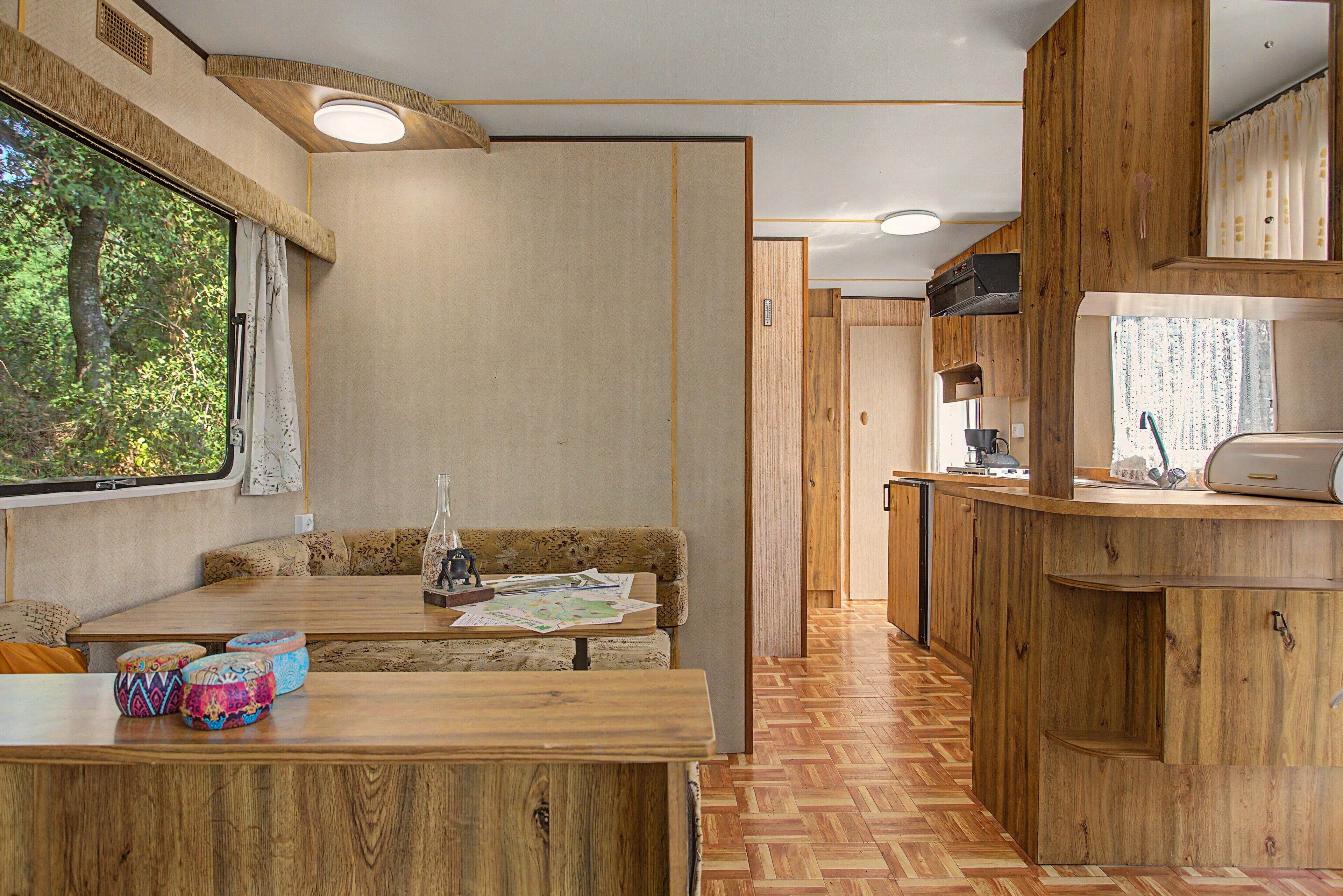 Ein kompaktes Wohnmobil-Interieur mit Küchenzeile, einer Sitzecke mit Tisch und einem Fenster mit Blick auf Grünflächen.