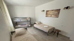 Et soveværelse med køjesenge, en enkelt seng, et lille bord og et billede på væggen.
