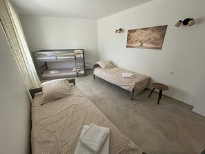 Ein Schlafzimmer mit Etagenbetten, einem Einzelbett, einem kleinen Tisch und einem Bild an der Wand.