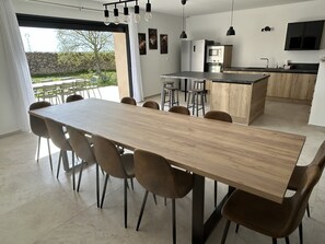 A modern kitchen with a central island, a dining area with a long table and chairs, and a view of the outdoors. - Spacious 5-bedroom house in Florensac with AC (Florensac)