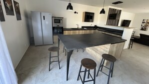 Et moderne køkken med en central ø, barstole, et køleskab, en ovn og hængende lamper.