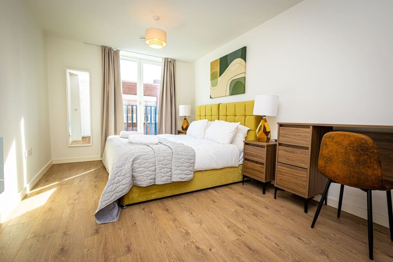 A bedroom with a bed, a desk, a chair, a lamp, and a window with curtains.