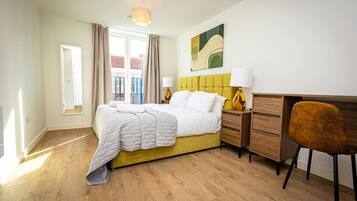 A bedroom with a bed, a desk, a chair, a lamp, and a window with curtains.