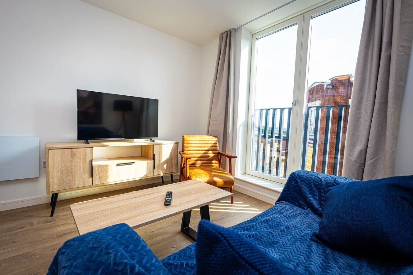 A modern living room with a flat-screen TV, wooden furniture, a sofa, and a balcony with curtains.