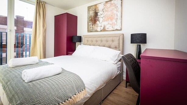 A hotel room with a bed, a desk, a chair, a red cabinet, a painting, and a view of the outside. - Birmingham City Retreat No 121 (Birmingham)