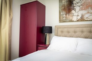 A hotel room with a large bed, a red wardrobe, a bedside table with a lamp, and a textured wall art piece. - Birmingham City Retreat No 121 (Birmingham)
