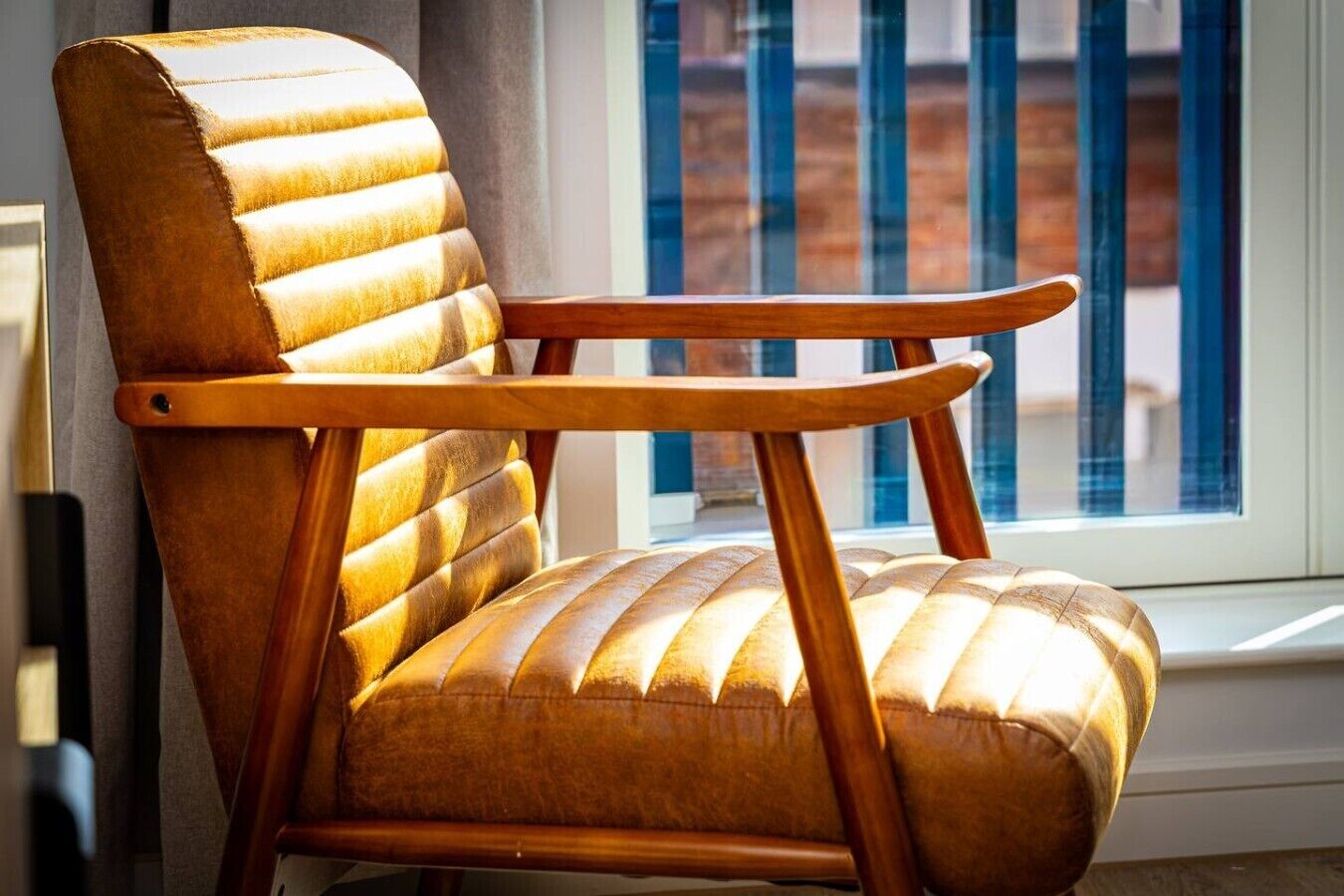 A chair with a high back and armrests, positioned near a window with a view of buildings.