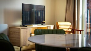 A hotel room with a flat-screen TV on a wooden cabinet, a round dining table with chairs, and a large window with curtains. - Birmingham City Retreat No 121 (Birmingham)