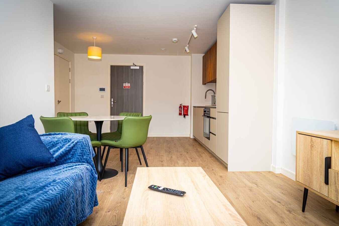 A compact living space with a bed, a dining table with chairs, a kitchenette, and a small cabinet.