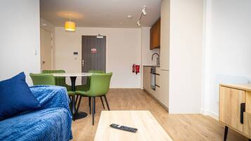 A compact living space with a bed, a dining table with chairs, a kitchenette, and a small cabinet.