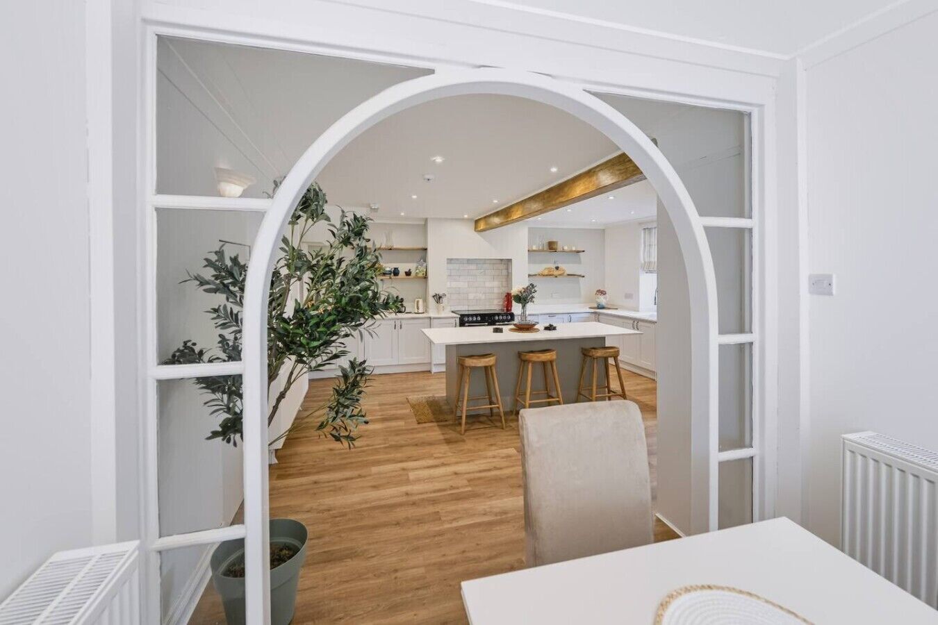 A modern kitchen with white cabinetry, a central island with stools, and a large plant.