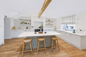 A modern kitchen with white cabinetry, a central island with stools, wooden beams on the ceiling, and a window with blinds. - Hobsland Farm nr Prestwick Airport (Monkton)