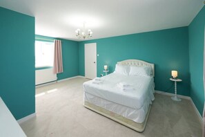 Een slaapkamer met blauwgroene muren, een wit bed, een kroonluchter en een nachtkastje met een lamp.