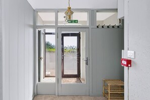 Eine graue Tür mit Glasfenster, ein grünes Ausgangsschild und ein rotes Notlichtgehäuse.