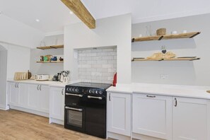 A modern kitchen with white cabinetry, a black stove, and wooden shelves above. - Hobsland Farm nr Prestwick Airport (Monkton)