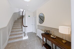 A hotel hallway with a carpeted staircase, a round mirror, a wooden console table with a lamp, and a sign indicating WiFi availability. - Hobsland Farm nr Prestwick Airport (Monkton)