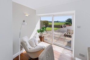 A room with a white sofa, a potted plant, and a view of a garden through a sliding glass door. - Hobsland Farm nr Prestwick Airport (Monkton)