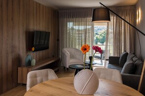A modern living room with a flat-screen TV, a round wooden table, a sofa, and a chair. - Krabo Luxury Suite (Vouliagmeni)