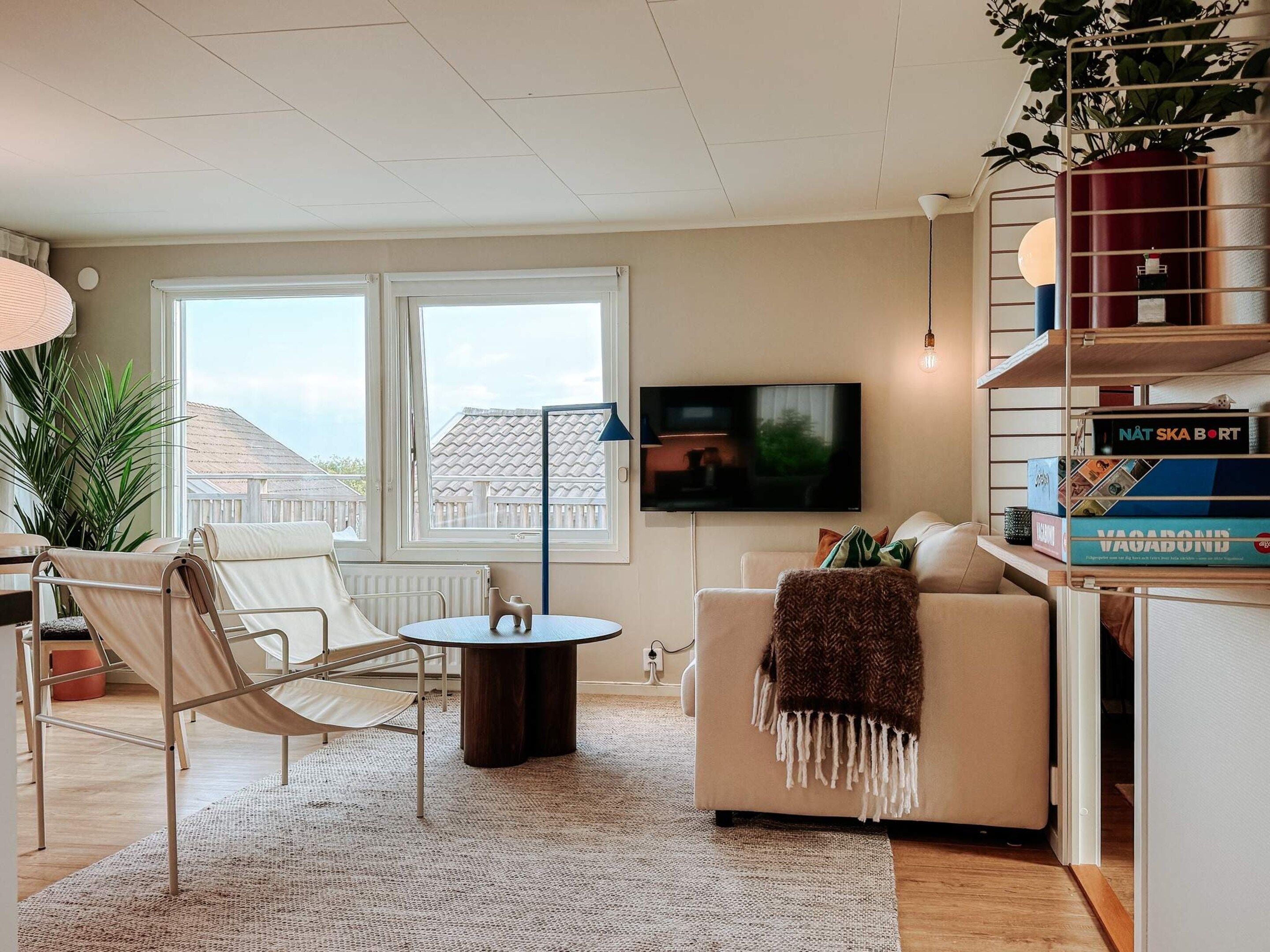 A living room with a sofa, a small round table, a hammock chair, a TV, and a bookshelf with books.