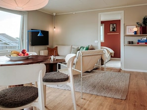 Una sala de estar moderna con comedor, sofá, televisor de pantalla plana y vista al exterior.