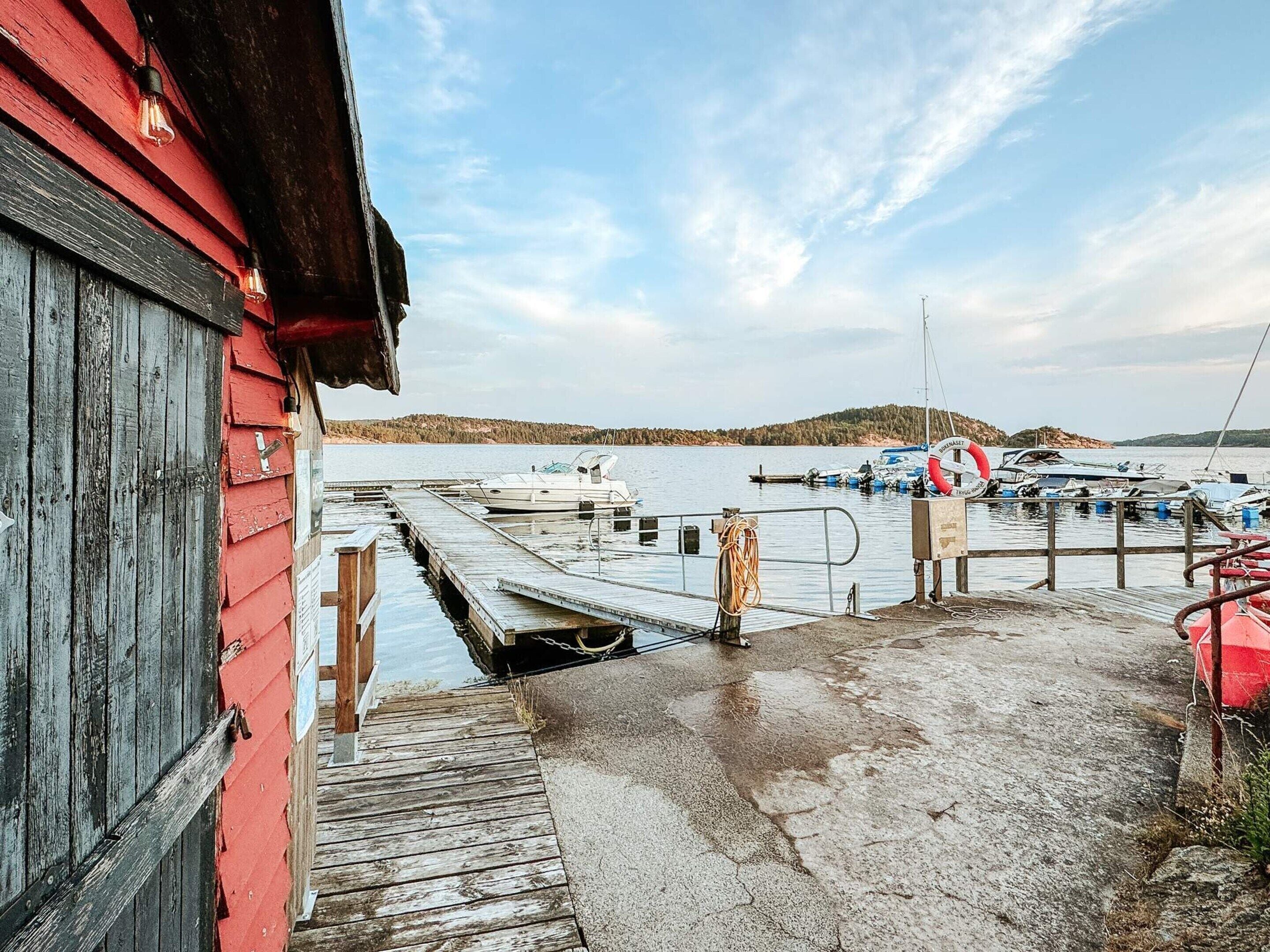 A wooden dock leading to a marina with boats, a lifebuoy, and a red building.