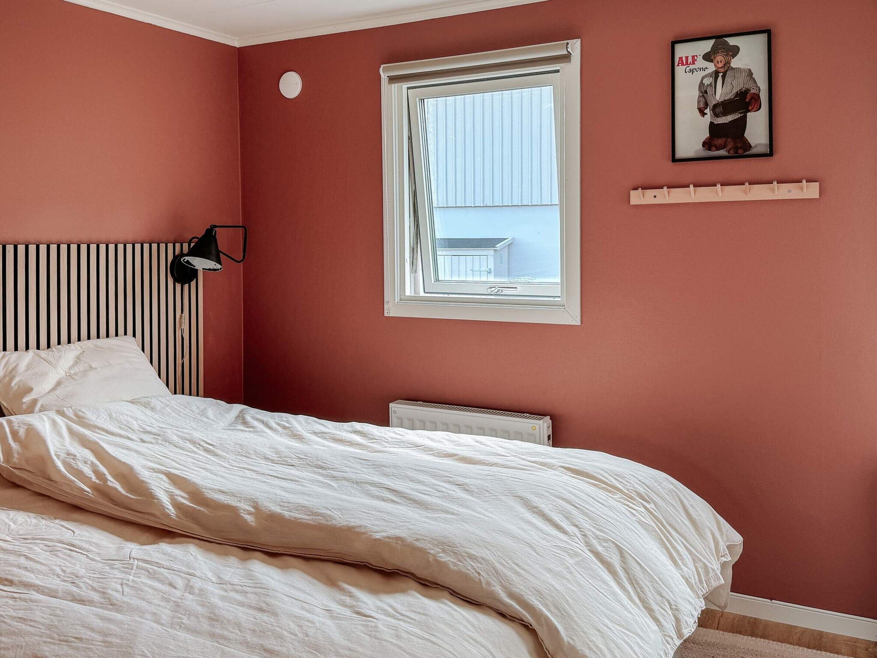 A bedroom with a bed, a radiator, a window, and a wall-mounted picture.