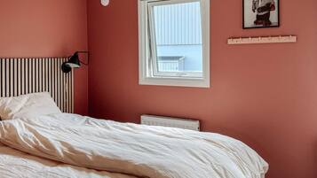 A bedroom with a bed, a radiator, a window, and a wall-mounted picture.
