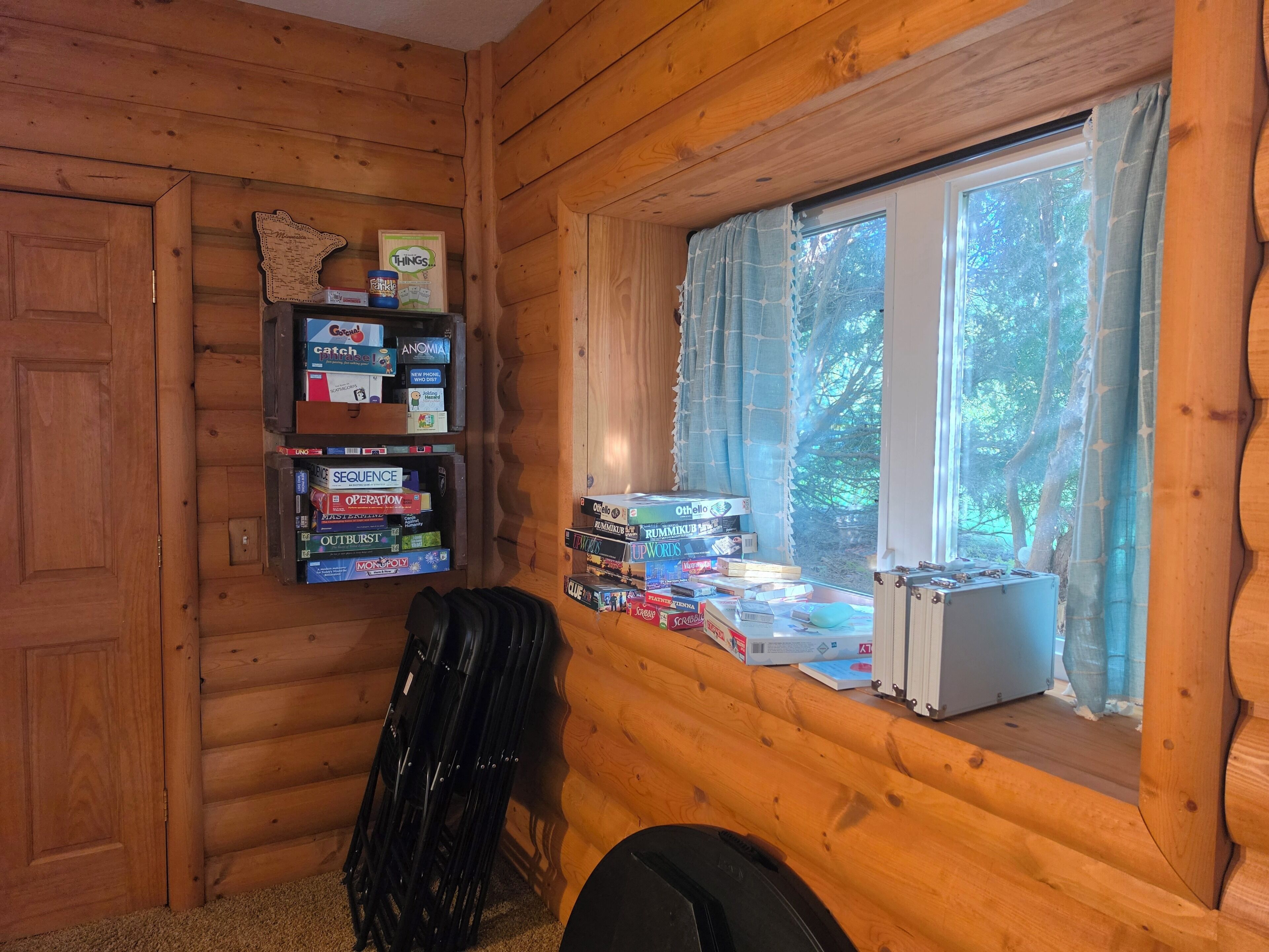 L’intérieur d’une cabane avec un mur en bois, une étagère remplie de jeux de société, une fenêtre avec des rideaux et un radiateur.