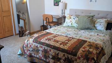 A bedroom with a large bed, a desk, a chair, a lamp, and a mirror.