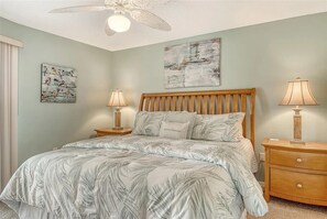 Ein Schlafzimmer mit einem Bett, zwei Nachttischen, einem Deckenventilator und Bildern an den Wänden.