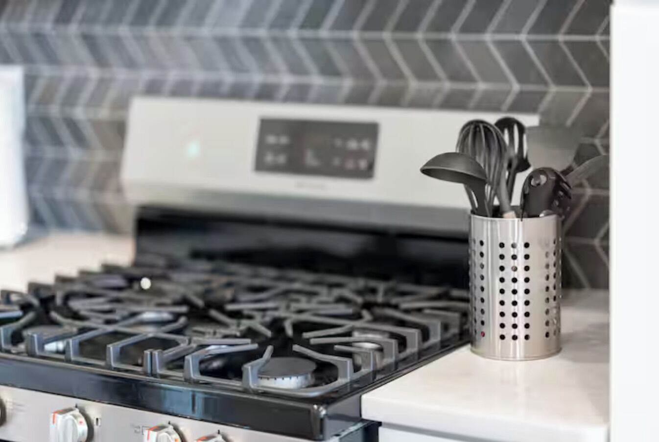 A kitchen with a gas stove, a stainless steel utensil holder, and a modern backsplash.