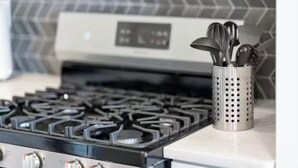 Una cucina con piano cottura a gas, portaoggetti per utensili in acciaio inossidabile e una schiena di colonna moderna.