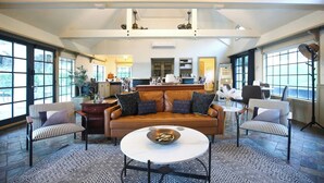 A spacious living area with a leather sofa, striped armchairs, a round coffee table, and large windows providing views of the kitchen and outdoor areas. - Ranch Estate/ Pool / Hot Tub / Family Reunions - Holiday Home (Moorpark)