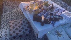 A picnic setup with a table, chairs, and a blanket on a patterned floor, with a sunset in the background. - Ranch Estate/ Pool / Hot Tub / Family Reunions - Holiday Home (Moorpark)
