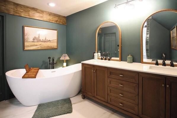 A bathroom with a freestanding bathtub, a vanity with a mirror, and a framed picture on the wall.
