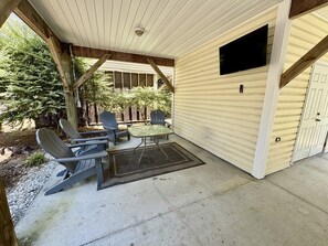 A covered patio with a table and chairs, a doormat, and a television mounted on the wall. - Ocean Lakes 3BR Beach House | Free Golf Cart | Sleeps 7 | Myrtle Beach (Myrtle Beach)