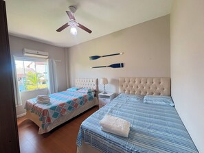 Ein Schlafzimmer mit zwei Betten, einem Deckenventilator, einem Fenster mit Vorhängen und Blick nach draußen.