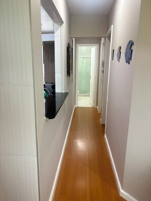 A hallway with a wooden floor, white walls, and a door leading to a bathroom. - Angra TOP View of the Mountain, Beach, Pool, Marina (Angra dos Reis)