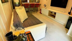 A modern living room with a sofa, a coffee table, a TV, and a kitchen in the background. - Casa Dez Guarajuba  (Camaçari)