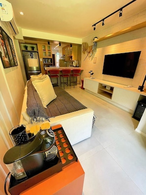 A modern living room with a sofa, a coffee table, a TV, and a kitchen in the background. - Casa Dez Guarajuba  (Camaçari)