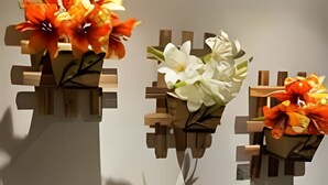 A bathroom with a wall-mounted sink, a framed certificate, and three flower arrangements in geometric containers.