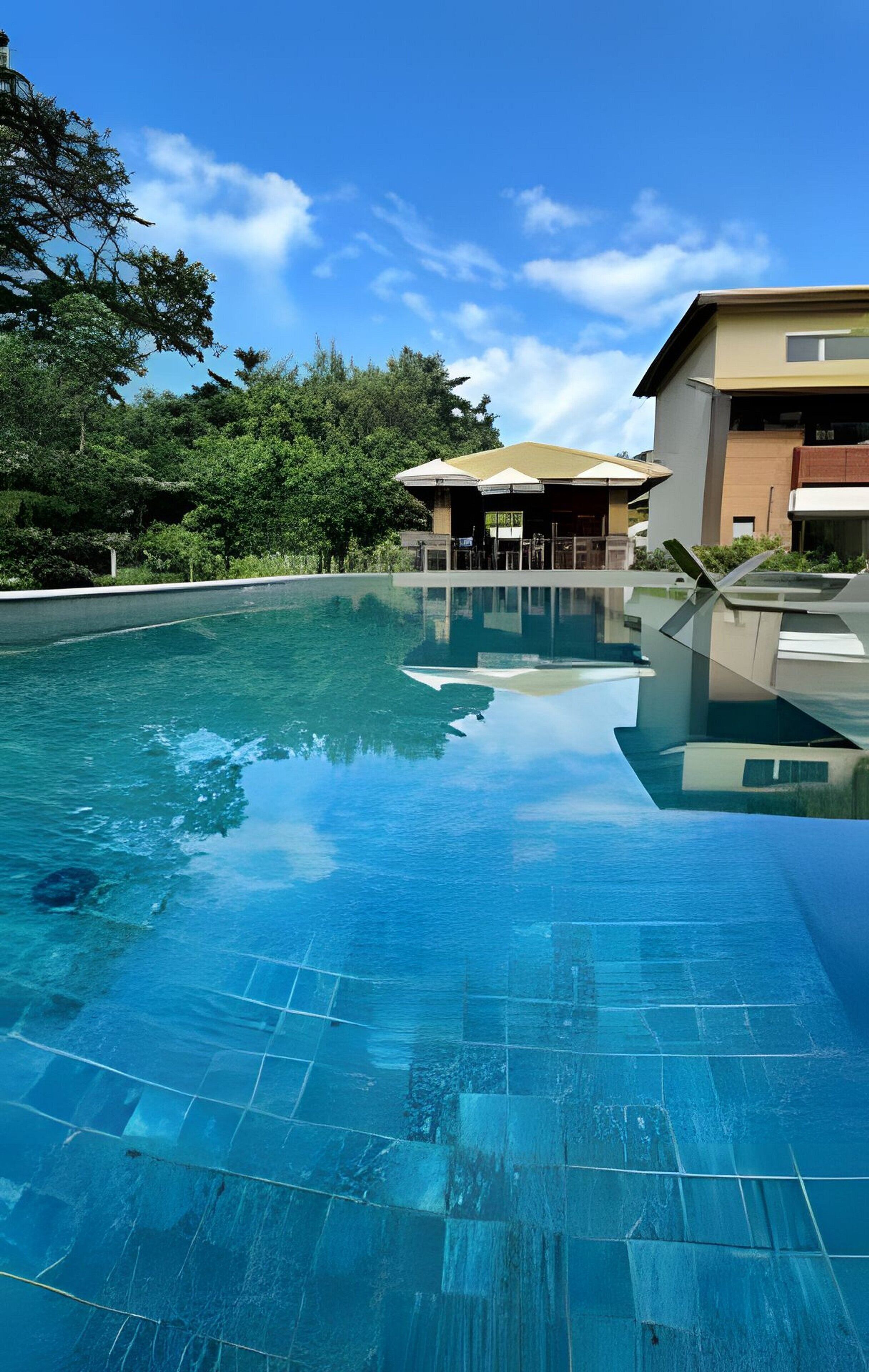 A swimming pool with a tiled deck, surrounded by greenery and buildings.
