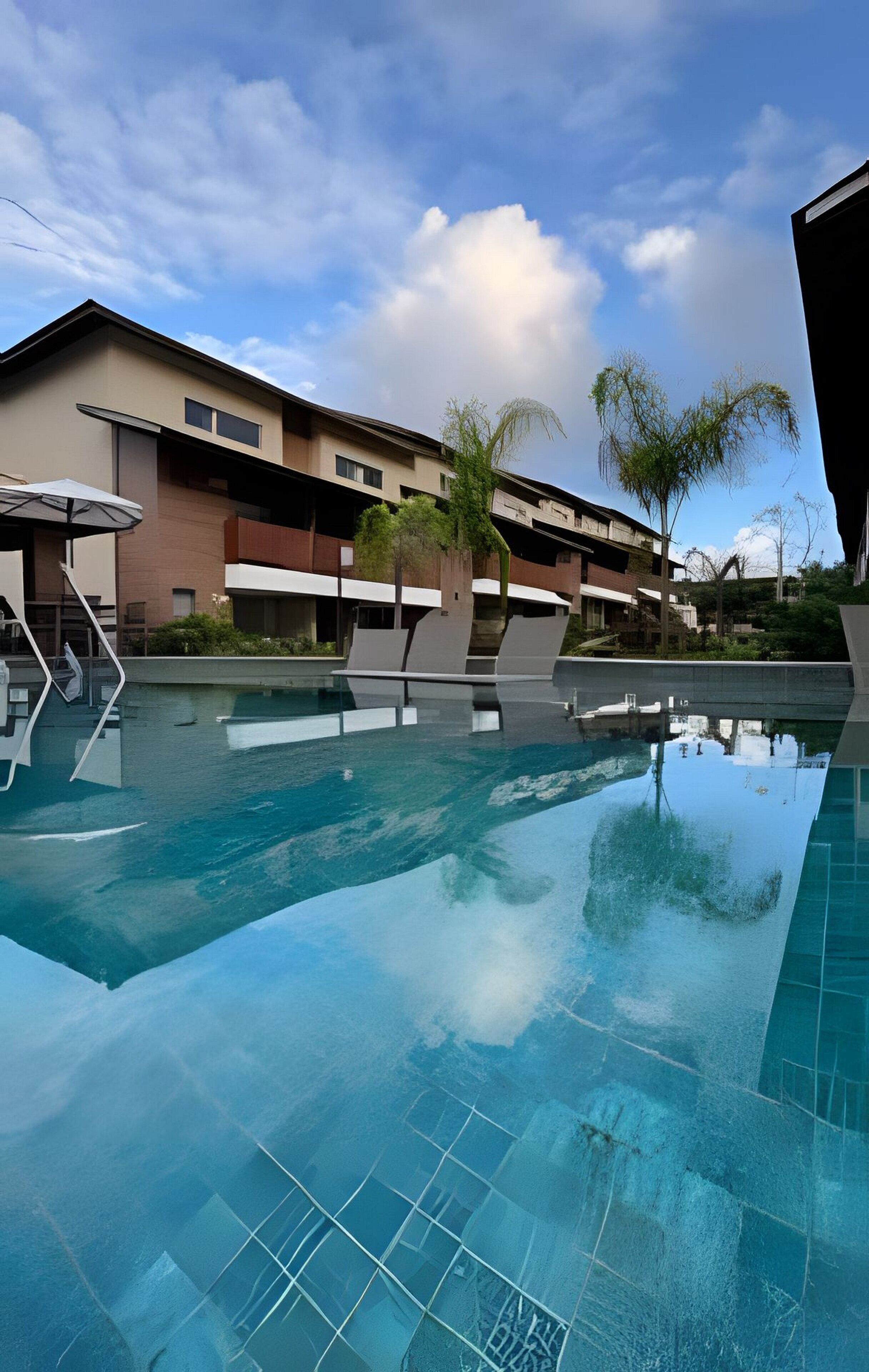 Ein Swimmingpool mit Liegestühlen, eine überdachte Sitzgelegenheit und im Hintergrund ein Gebäude mit mehreren Balkonen.
