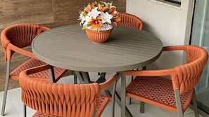 A round table with a potted plant in the center, surrounded by four orange chairs with a woven pattern. - Casa Dez Guarajuba  (Camaçari)