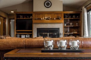 A living room with a brown leather couch, a fireplace, and three candles on a tray. - Lakepoint Overlook | Dock + Lake Access (Bella Vista)